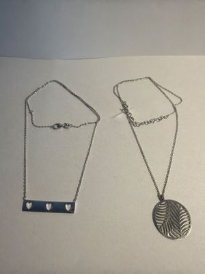 two silver necklaces on a white surface with a heart pendant