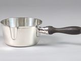 une saucière en argent avec un manche en bois, posée sur un plan de travail blanc