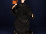 an old fashioned doll with a black dress and a red hat