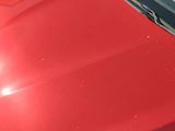 the front end of a red car with a denting dent on it ' s hood