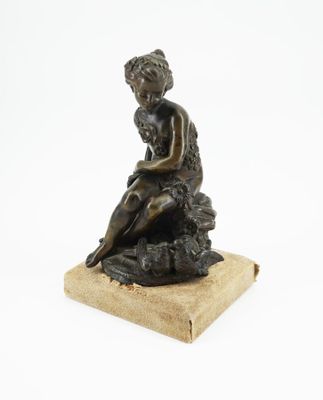 une vieille statue en bronze représentant un garçon assis sur un rocher