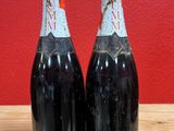 two bottles of wine sitting on top of a wooden table next to a red wall