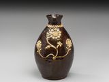 vase marron et doré orné de fleurs et de feuilles sur fond gris