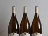 three bottles of wine sit on a wooden table in front of a wall
