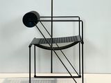 une chaise noire et une lampe noire posées sur un sol blanc