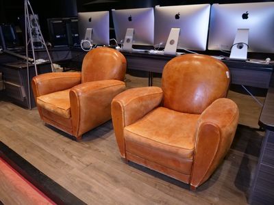 deux fauteuils en cuir marron dans une pièce où des ordinateurs sont accrochés au mur