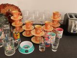 de nombreuses tasses et soucoupes posées sur une table où se trouvent un grille-pain et un autre grille-pain