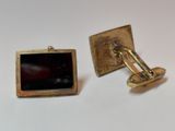 pair of gold tone cufflinks with a black glass in the center