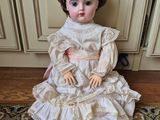 doll sitting on a rug in front of a door wearing a hat and dress