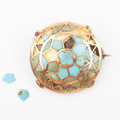 turquoise and gold broochle on a white surface with broken glass