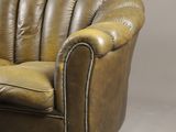 brown leather sofa with brown wood legs and arm rests against a gray wall