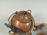 a small copper teapot with a handle on a white table