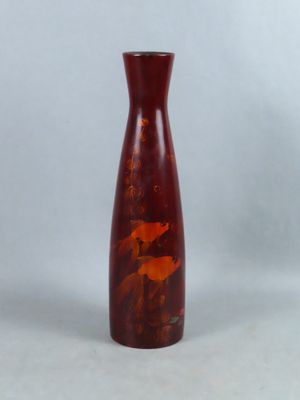 un vase rouge posé sur une table près d'un mur blanc