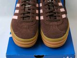 des baskets Adidas marron avec des bandes roses, posées sur une boîte bleue