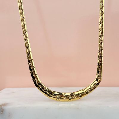 un collier à chaîne en or posé sur un bloc de marbre
