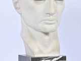 un buste en marbre blanc représentant un homme aux cheveux bouclés, posé sur un socle en marbre noir