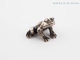 a close up of a silver frog on a white surface