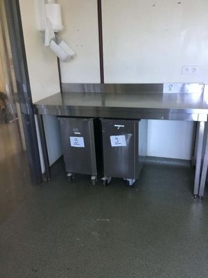 two stainless steel tables in a kitchen with two trash cans