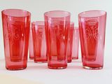 six red glasses lined up on a white surface
