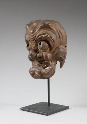 un masque en bois posé sur un socle noir, avec un fond blanc