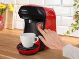 la main d'une femme tendue vers une tasse de café devant une cafetière rouge