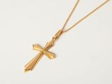 un pendentif en forme de croix en or, suspendu à une chaîne en or, sur fond blanc