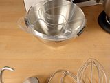 a box with a mixer, a bowl, a whisk and a whisk attachment on a wooden table