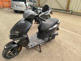un scooter garé sur un parking, avec une voiture en arrière-plan