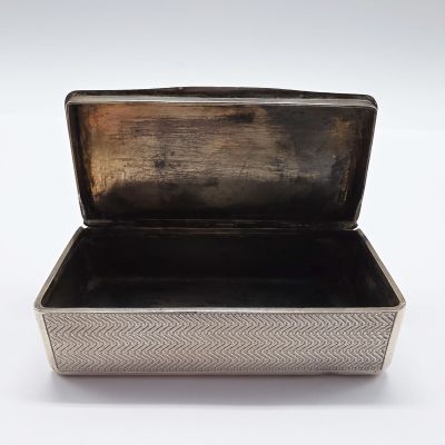 une vieille boîte en argent posée sur une surface blanche, le couvercle ouvert