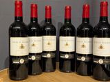 six bottles of red wine are lined up on a wooden barrel