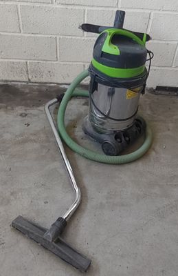 un aspirateur vert et noir posé par terre, à côté d'un mur de briques blanches