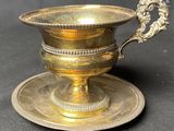 une tasse et une soucoupe en laiton ancien posées sur une assiette à sauce