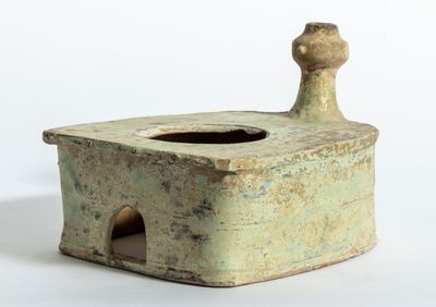 un petit vase vert muni d'une anse en bois, posé sur une surface blanche