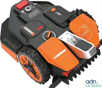 an orange and black robotic lawn mower sitting on top of a white surface