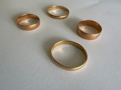 three gold wedding rings on a white table with a white background
