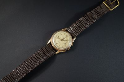 une image représentant une montre en or avec un bracelet en cuir marron sur un fond noir