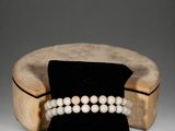 a close up of a bracelet with pearls on a wooden stand