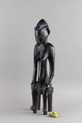 une photo représentant la statue d'un homme assis sur un tabouret