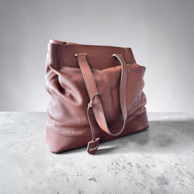 un sac à main en cuir marron posé sur une surface en béton, avec un mur blanc en arrière-plan