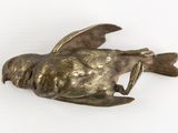 a bronze bird that is laying down on a white surface