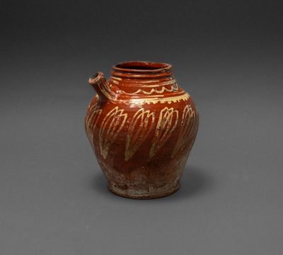 an old brown vase with a handle sitting on a gray surface