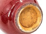 a red vase with a brown lid sitting on a white surface
