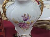 un vase blanc posé sur une table où se trouvent des assiettes et un cadre photo