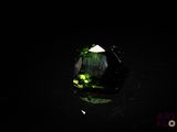un gros plan d'une tourmaline verte posée sur une surface noire