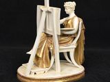 an image of a figurine of a woman sitting at a easel