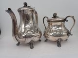 two silver teapots and a coffee pot sitting on a table