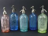 Quatre bouteilles en verre de couleurs différentes sont alignées sur une surface noire.