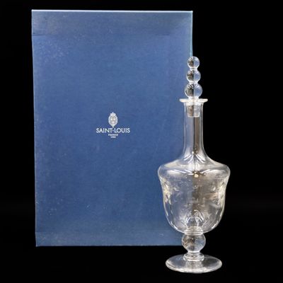 une bouteille en verre transparent avec un bouchon argenté, posée devant une boîte bleue
