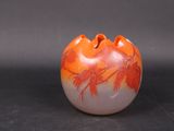 un vase orange et blanc orné de feuilles, posé sur une surface noire