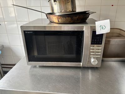 un micro-ondes argenté posé sur un plan de travail, avec une casserole dessus